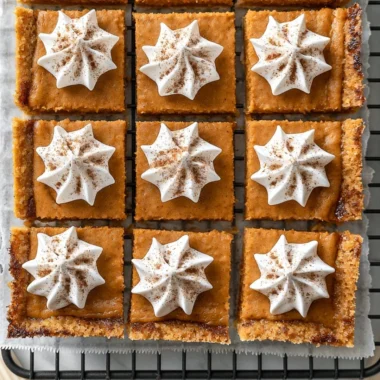 Delicious cozy pumpkin pie bars on a plate topped with whipped cream.