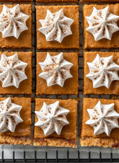 Delicious cozy pumpkin pie bars on a plate topped with whipped cream.