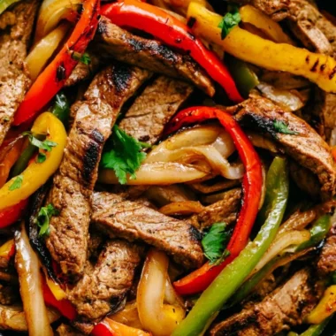 Delicious skillet steak fajitas sizzling in a cast iron pan with colorful peppers and onions.