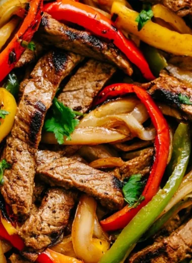 Delicious skillet steak fajitas sizzling in a cast iron pan with colorful peppers and onions.